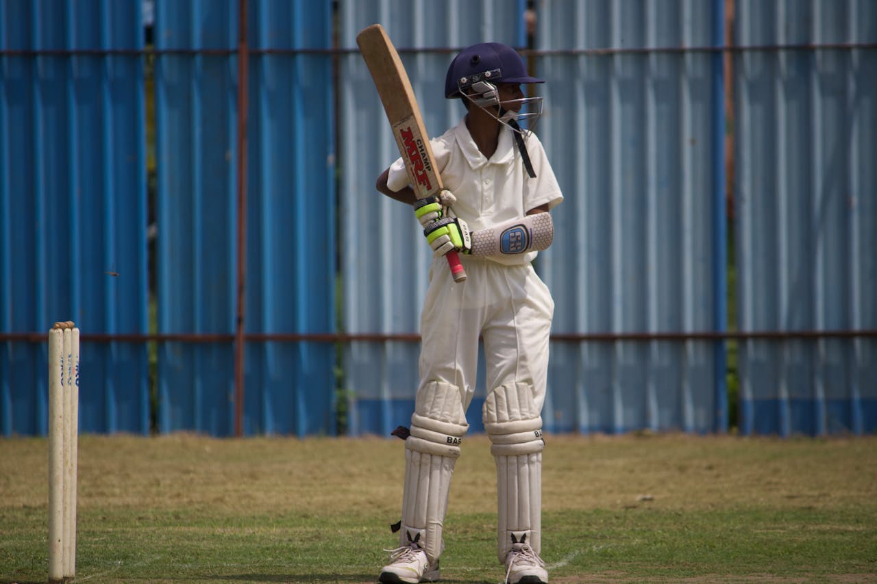 Youth cricket player in protective gear poised to bat during a sunny day on the field.
